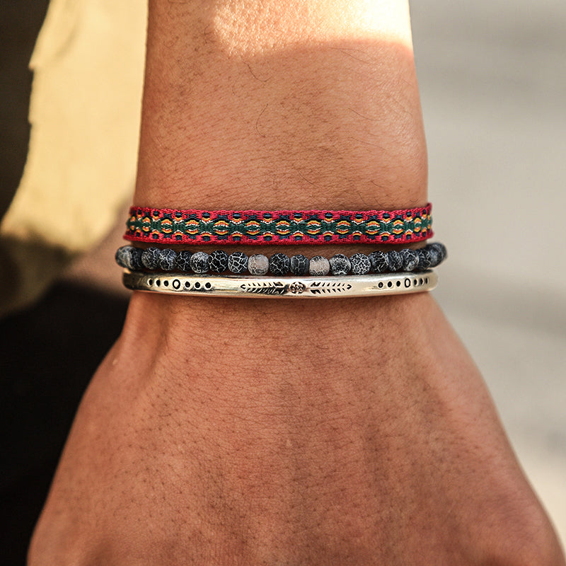 Ensemble de trois bracelets tibétains pour homme : un bracelet en fil rouge avec motifs, un bracelet de perles en apatite grise et un jonc en argent gravé.