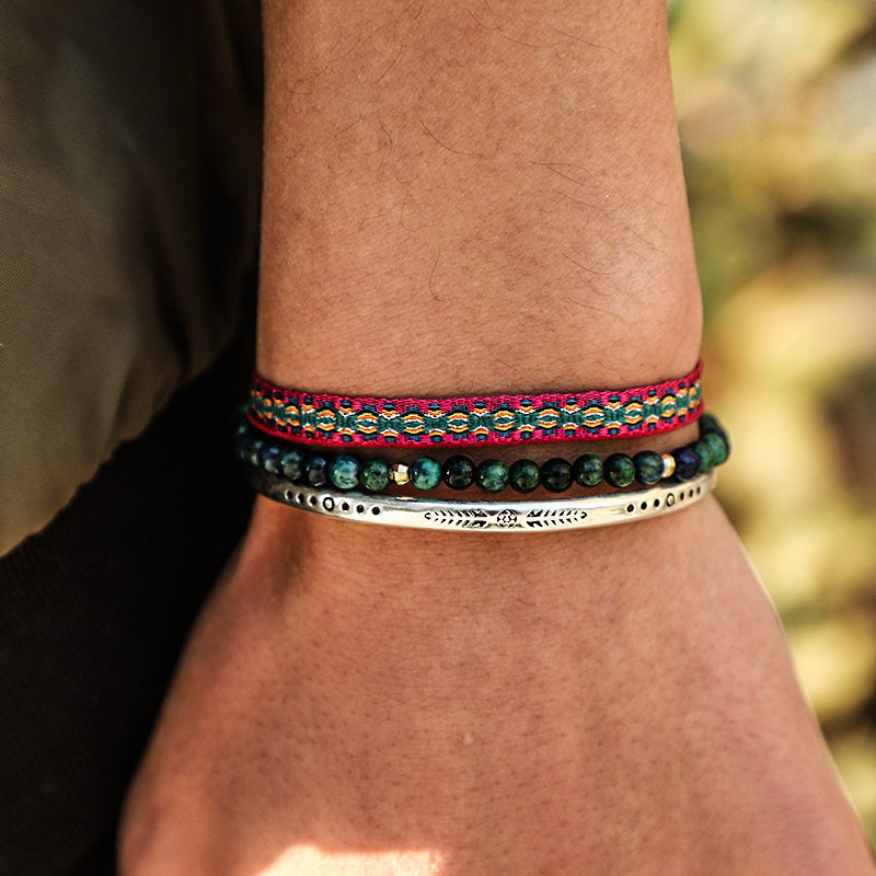 Bracelet Tibétain Trio Vitalité composé de 3 bracelets : un bracelet ruban rouge et vert orné de motifs géométriques, un bracelet de perles vertes et un bracelet jonc argenté gravé de symboles ethniques.