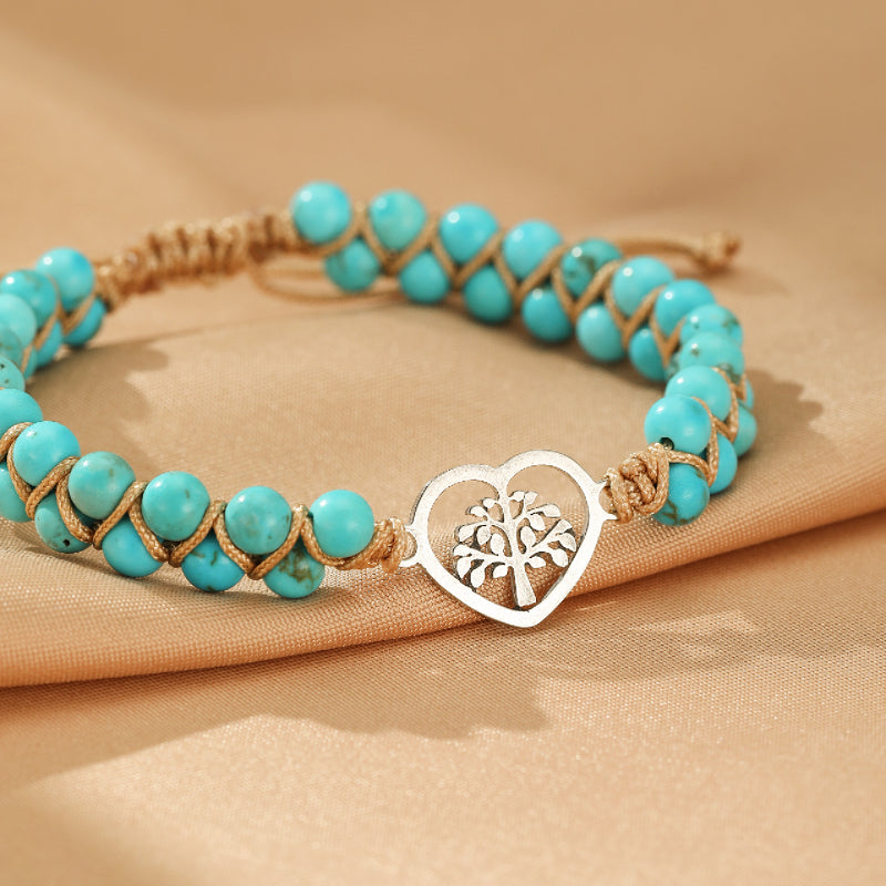 Bracelet en turquoise avec un pendentif en forme de cœur contenant un arbre de vie stylisé, monté sur un cordon tressé.