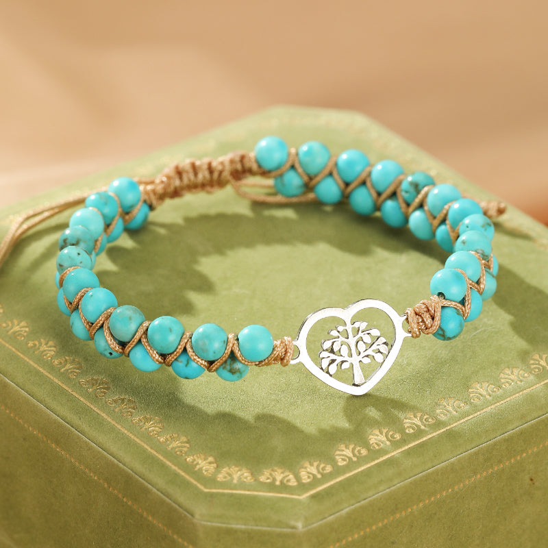Bracelet turquoise avec un pendentif en forme de cœur ajouré sur lequel est sculpté un arbre de vie, sur un fond vert.