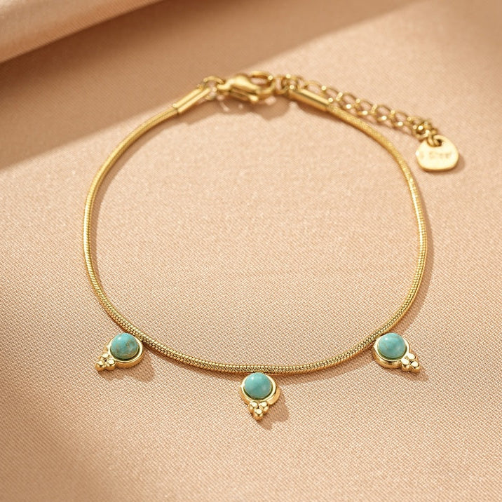 Bracelet en plaqué or avec trois petites pierres turquoise rondes serties sur une chaîne serpent délicate. Le fermoir est un mousqueton avec une petite extension de chaîne et un breloque en forme de cœur.