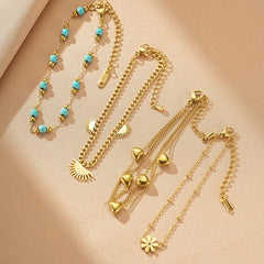 Ensemble de quatre bracelets en or, dont un avec des perles turquoise, un avec des soleils, un avec des cœurs et un avec une fleur.