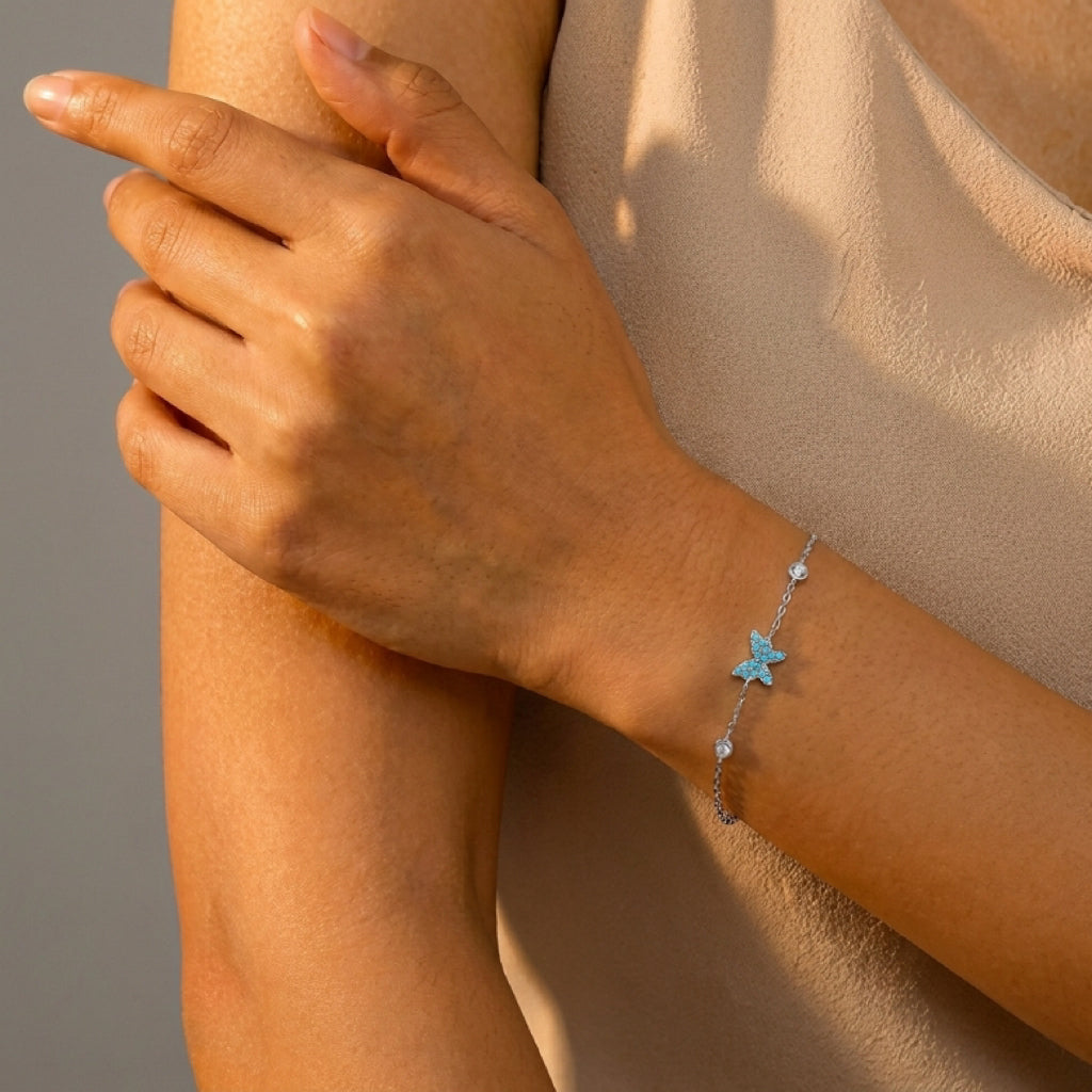 Bracelet en argent avec un motif papillon bleu turquoise incrusté et de petites pierres scintillantes, porté au poignet d'une femme.