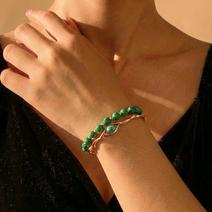 Bracelet turquoise avec des perles vertes et un fermoir en forme d'œil, porté sur le poignet d'une femme.