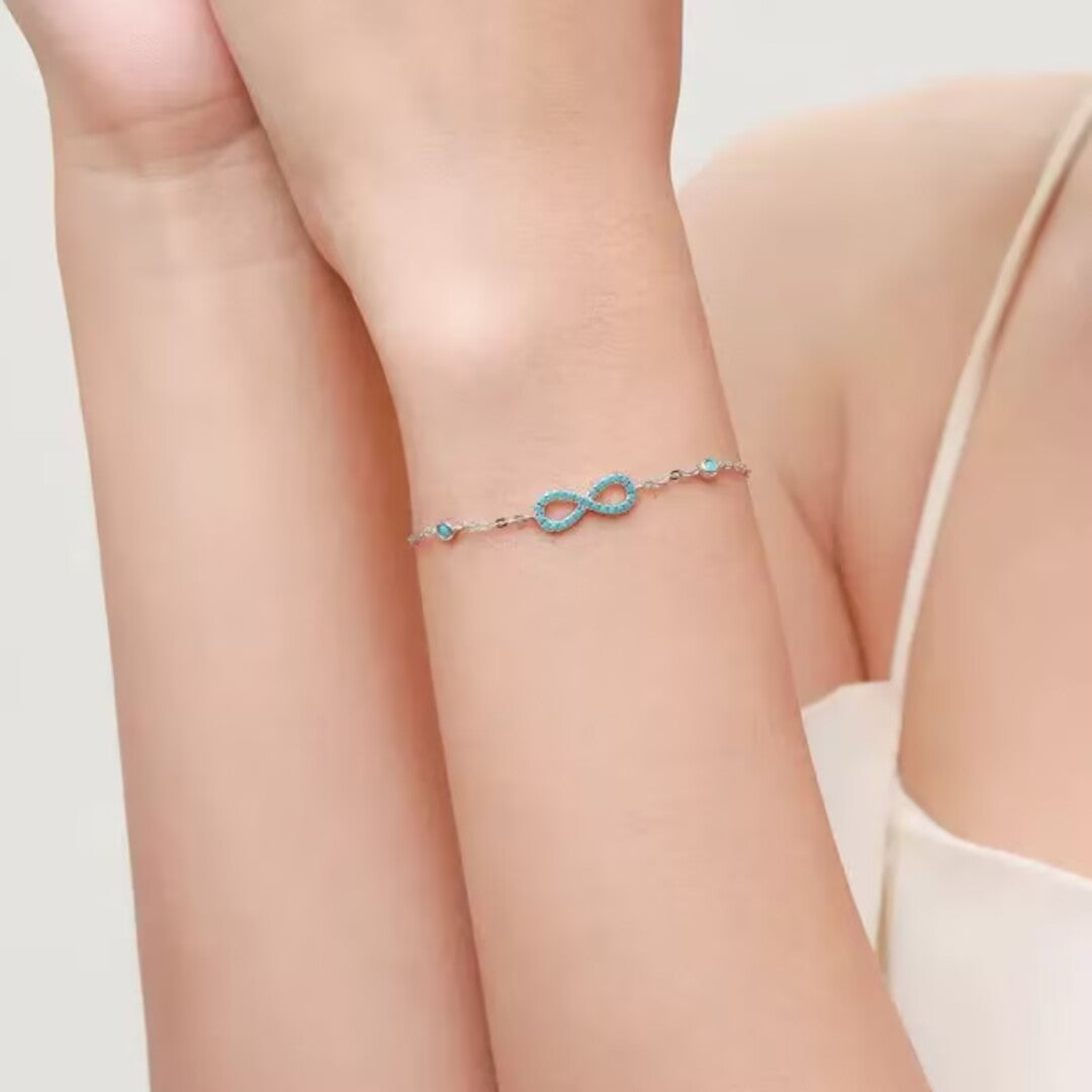 Bracelet jonc en argent 925, orné d'un symbole infini serti de petites pierres turquoise bleues, posé sur le poignet d'une femme.