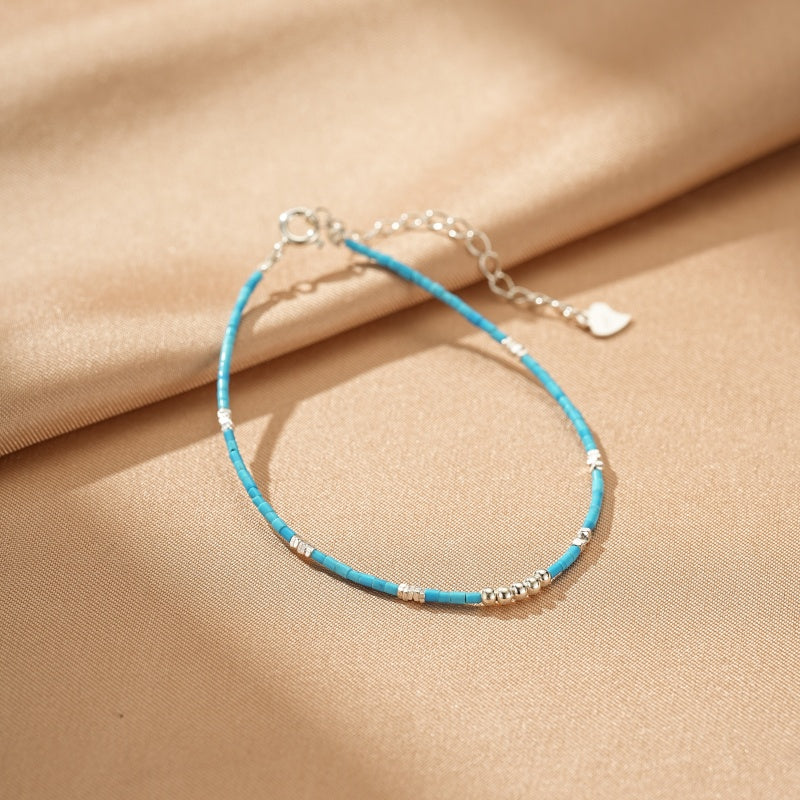 Bracelet fin en argent avec des petites perles turquoise et des éléments argentés, doté d'un fermoir réglable et d'un petit pendentif cœur.