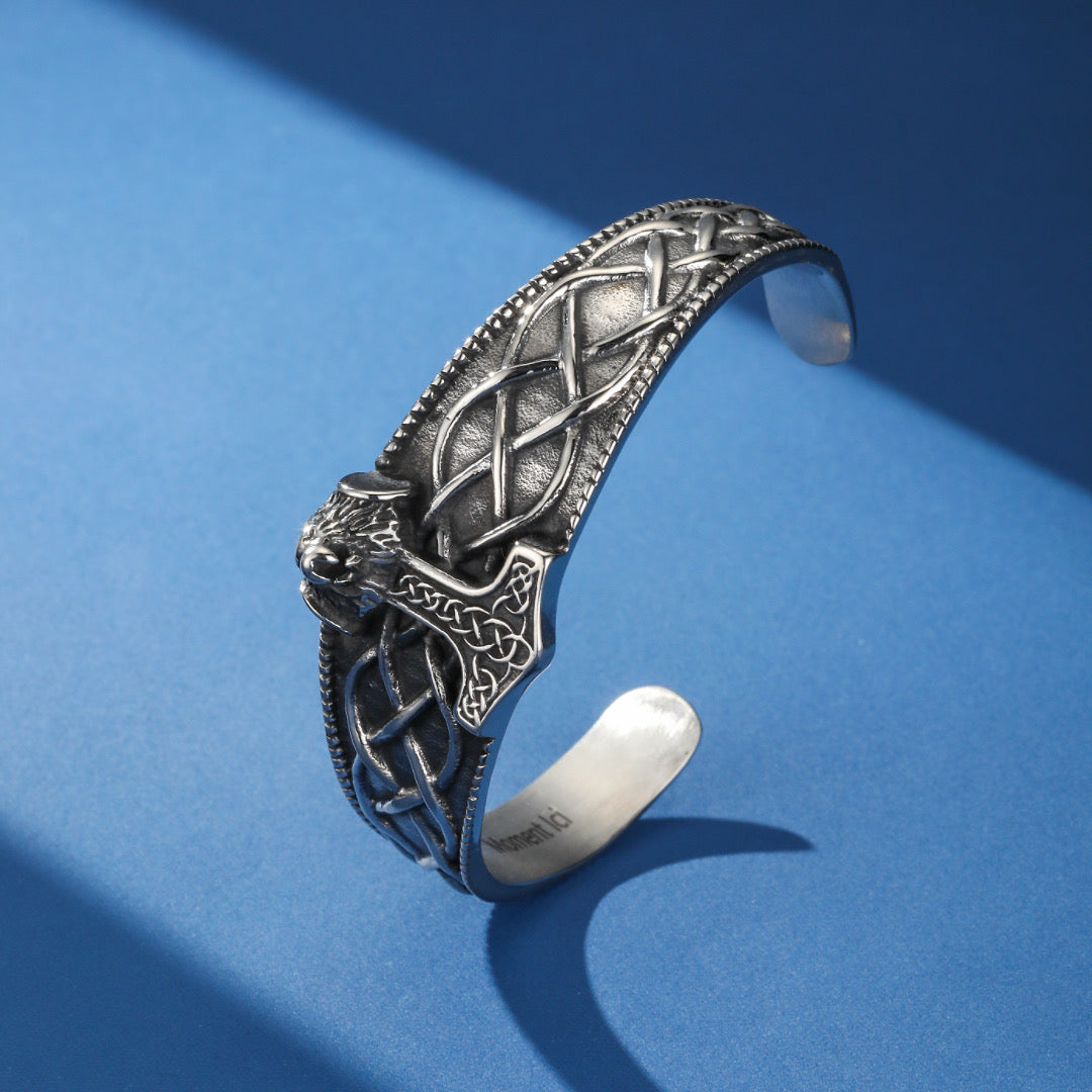 Bracelet jonc viking en métal argenté orné du marteau de Thor stylisé et de motifs celtiques entrelacés, sur fond bleu.