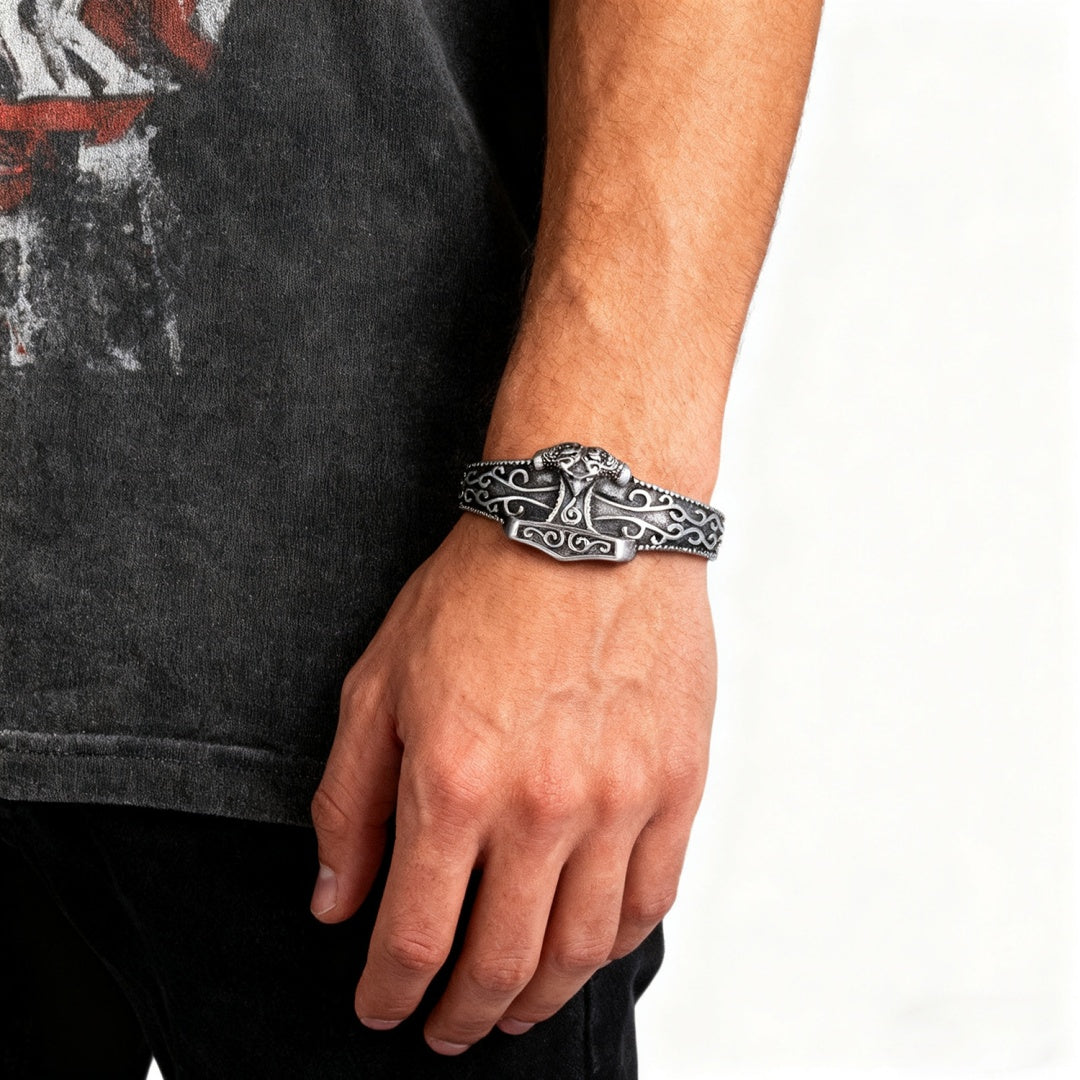Bracelet jonc viking en argent avec un marteau de Thor stylisé et des motifs entrelacés, porté au poignet d'un homme.