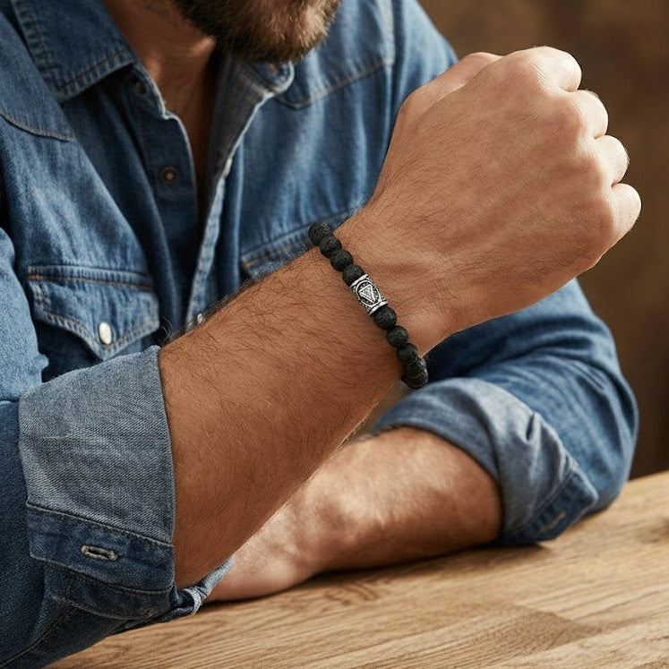 Bracelet viking en pierre de lave noire avec un fermoir argenté orné d'un symbole tribal stylisé, porté au poignet d'un homme.