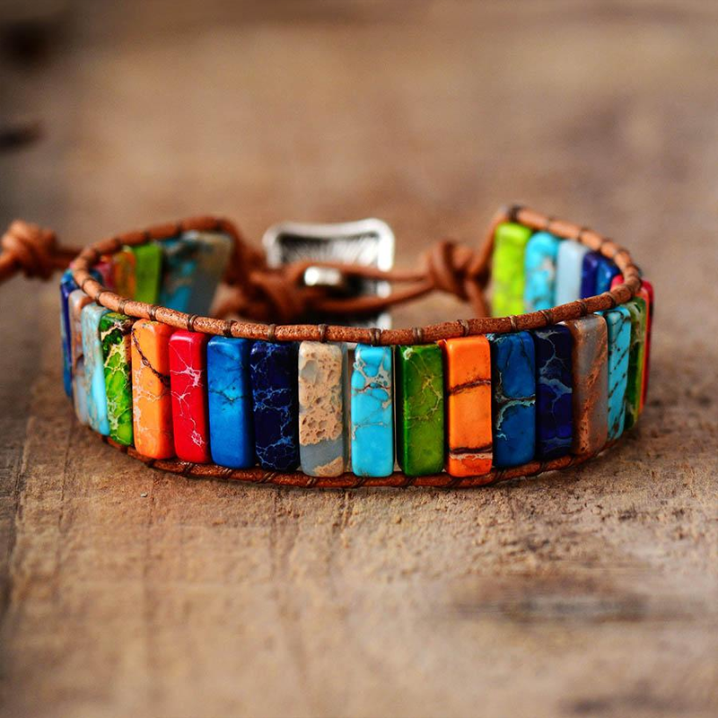 Bracelet jonc en cuir brun avec des pierres rectangulaires de 7 chakras colorées, posé sur un fond en bois