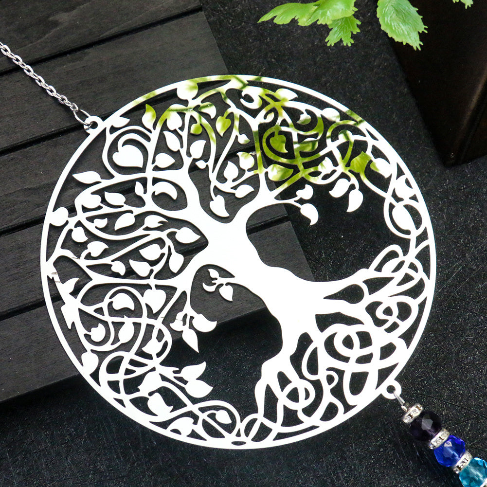Capteur de soleil Arbre de Vie blanc ajouré avec des feuilles vertes stylisées et des perles bleues et violettes suspendues, sur un fond sombre.