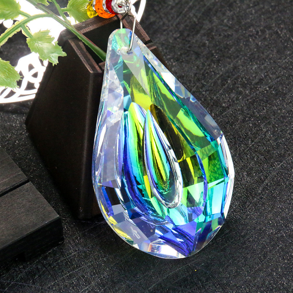 Goutte de cristal prismatique aux reflets bleus, verts et jaunes, suspendue à un fil métallique, évoquant un capteur de soleil Arbre de Vie.