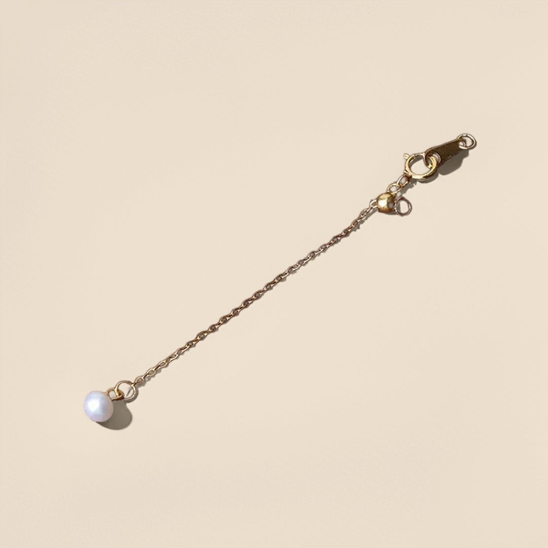 Chaînette d'extension en argent avec une petite perle nacrée à son extrémité, vue de haut sur fond beige.