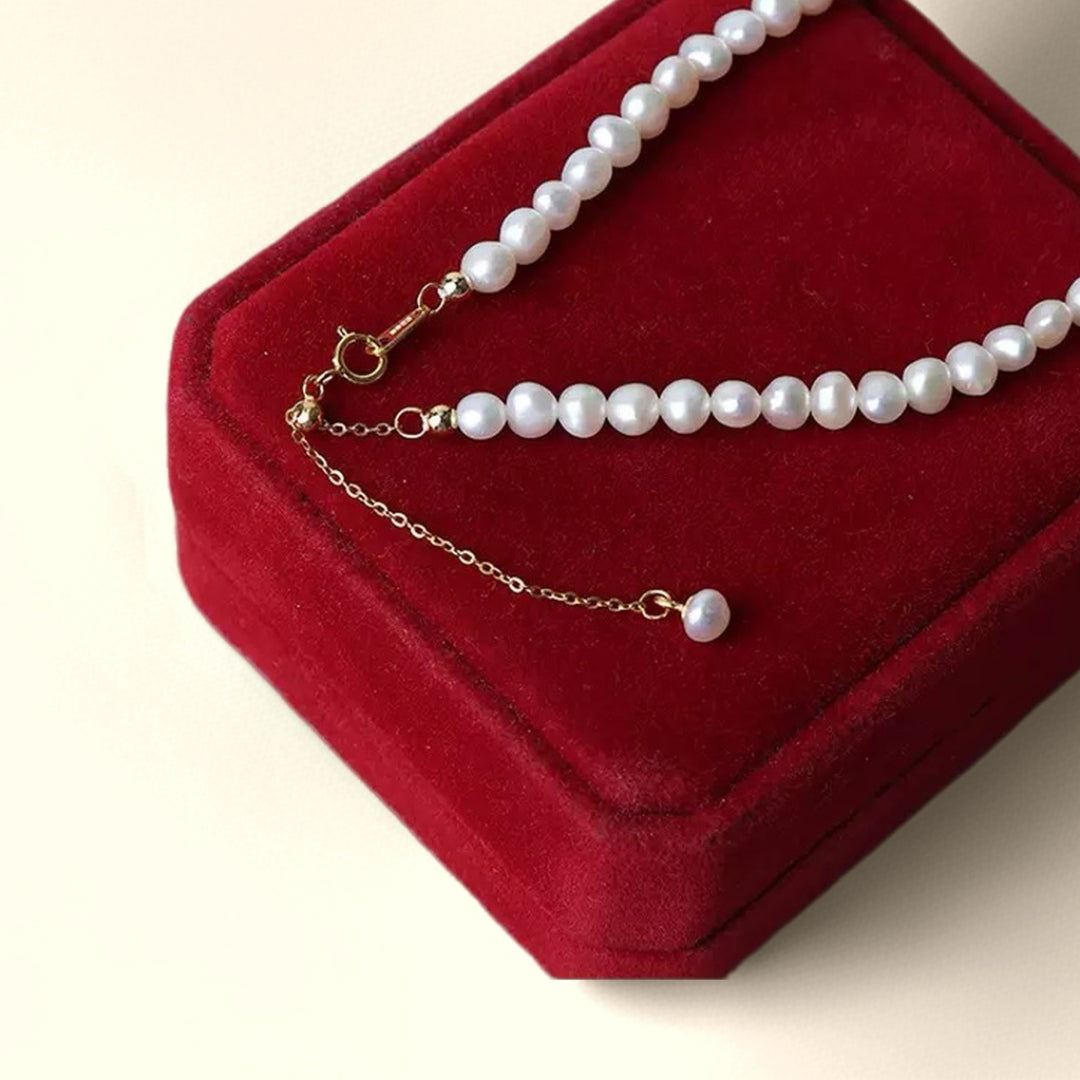 Gros plan sur une chaîne d'extension de bracelet en argent ornée de petites perles blanches et d'une perle unique à son extrémité, posée sur un écrin en velours rouge.