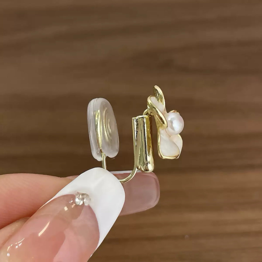 Clip d'oreille en forme de fleur avec perle et pétale blanc, monture dorée et coussinet transparent, vue rapprochée.