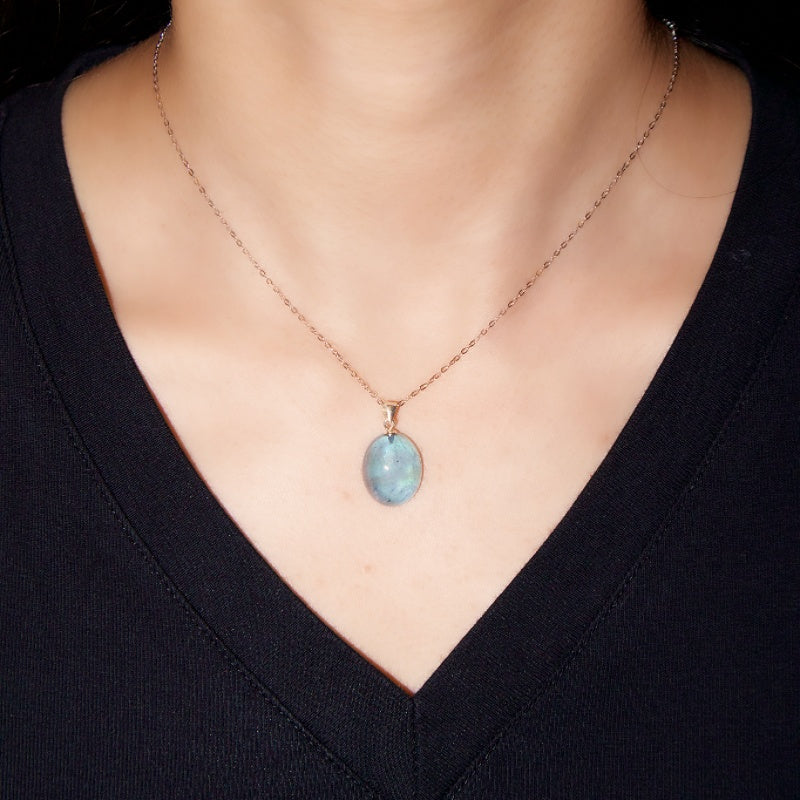 Collier avec un pendentif ovale en aigue-marine bleutée sur une fine chaîne en argent, porté sur un haut noir.