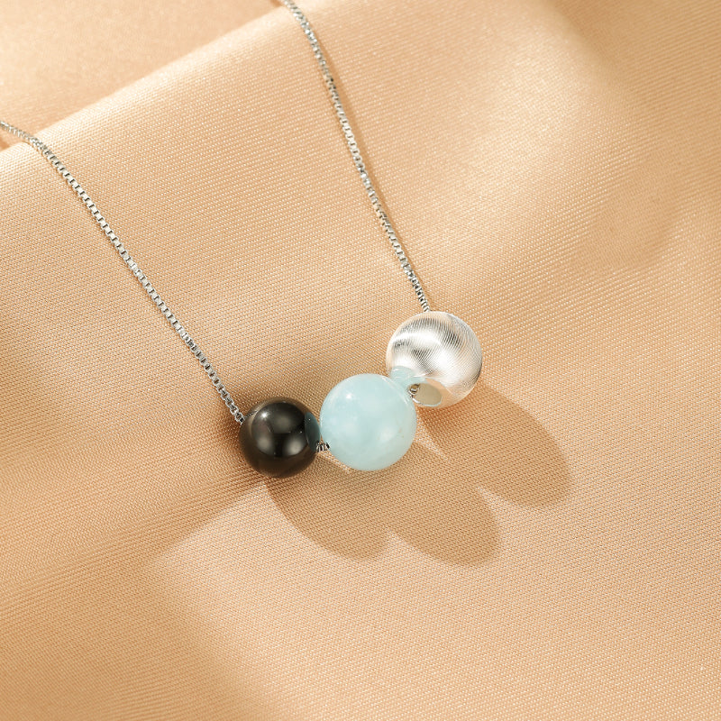 Collier Onde Lumineuse en argent 925, orné de perles rondes d'aigue-marine bleu clair, d'obsidienne noire et d'une perle texturée en argent, le tout sur une chaîne fine.