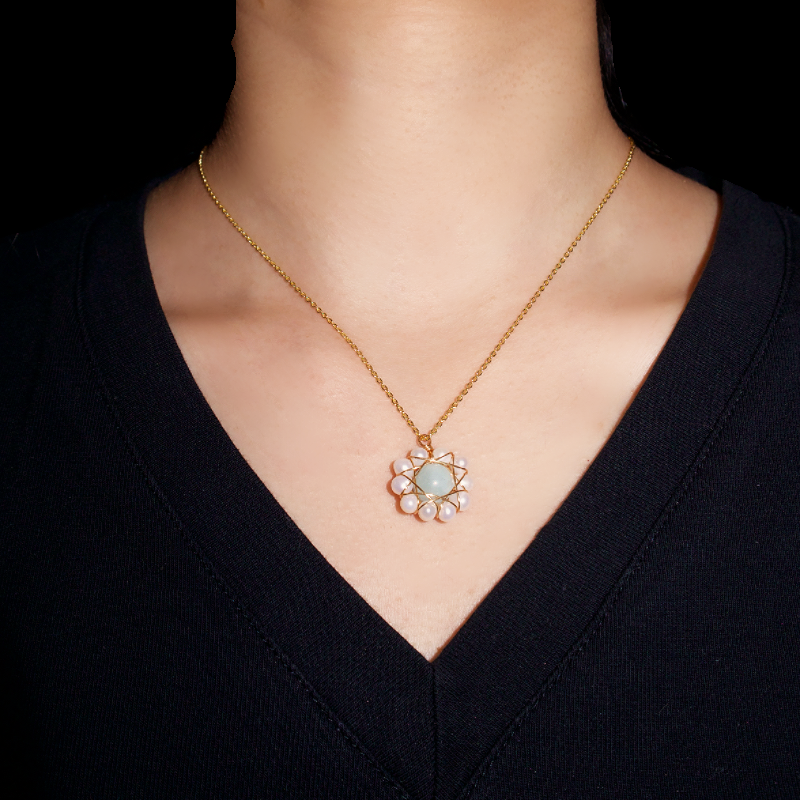 Collier "Harmonie des Mers" avec un pendentif central en aigue-marine pâle, entouré de petites perles blanches formant des pétales autour du centre, sur une chaîne dorée fine portée par une femme.