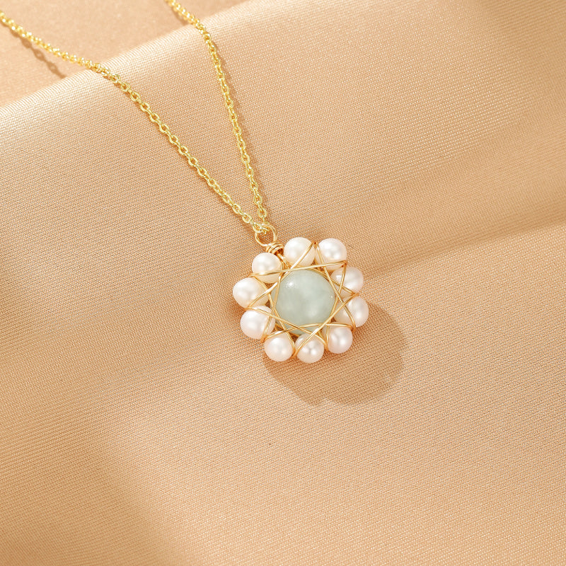 Collier Harmonie des Mers avec un pendentif rond bleu clair entouré de perles blanches, monté sur une chaîne dorée, sur un fond beige satiné.