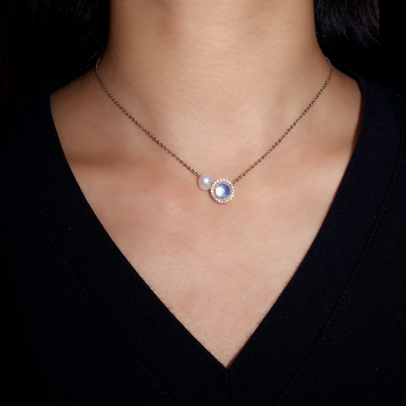 Collier "Harmonie Heureuse" en argent 925 avec une pierre bleue ronde entourée de petits cristaux et une perle blanche nacrée, porté par une femme.