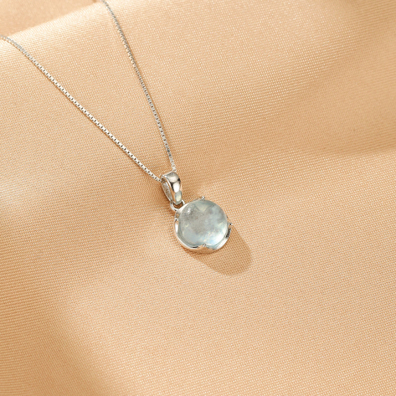 Collier pendentif aigue-marine bleu clair en argent 925, chaîne fine, sur fond satiné beige.