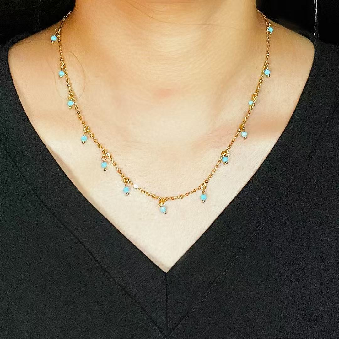 Collier fin en plaqué or orné de petites gouttes d'amazonite bleu clair, porté par une femme.