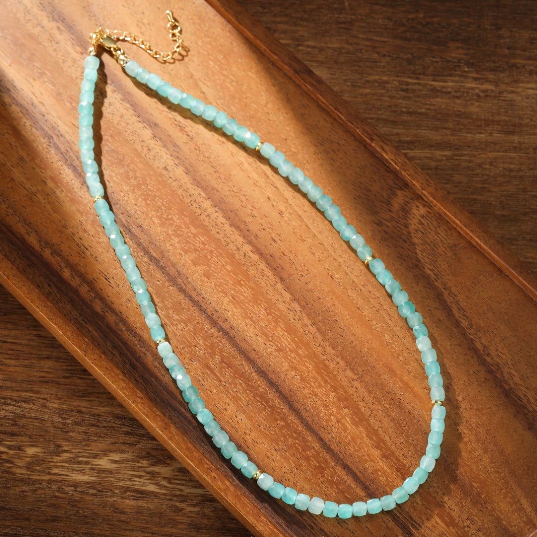 Collier en amazonite naturelle aux nuances bleutées et vertes, avec de petites perles dorées, posé sur un plateau en bois.