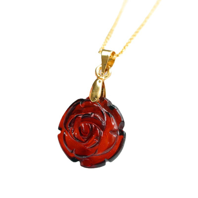 Collier Ambre Lumière d’Automne avec un pendentif en forme de rose rouge sculptée sur une chaîne en or, sur fond blanc.