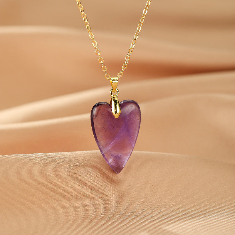 Collier avec un pendentif en forme de cœur en améthyste sur une chaîne dorée, sur fond satiné beige.