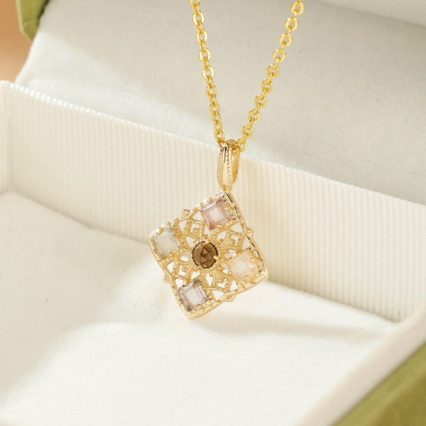 Collier plaqué or avec un pendentif carré mosaïque incrusté de petites pierres de couleur, dont une pierre brune au centre, présenté dans son écrin.