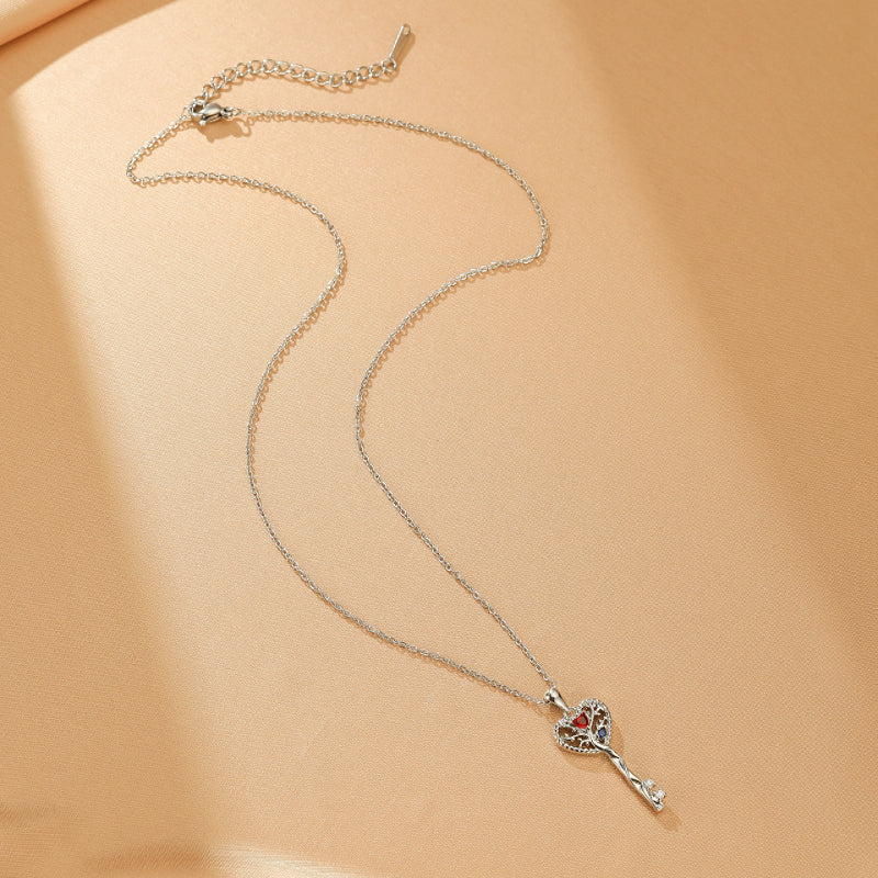Collier Arbre de Vie en argent avec un pendentif en forme de clé orné d'un cœur rouge au centre et d'une petite pierre blanche à l'extrémité.