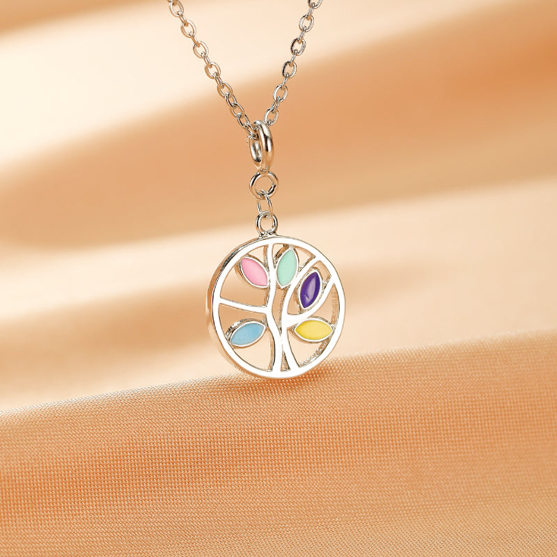 Collier Arbre de Vie en argent avec des feuilles colorées rose, bleu, vert, violet et jaune, sur fond beige doux.