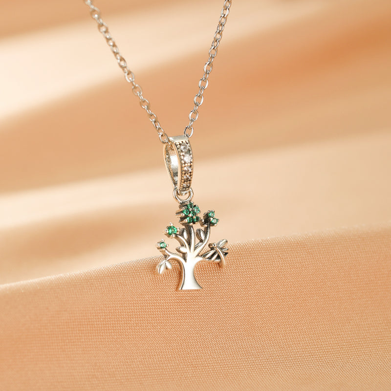 Collier Arbre de Vie en argent avec des feuilles vertes serties de pierres, pendentif délicat sur fond beige satiné.