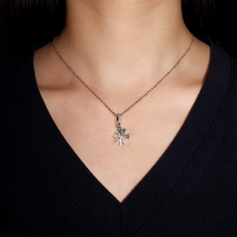 Collier Arbre de Vie en argent avec des pierres vertes, porté par une femme sur un haut noir.