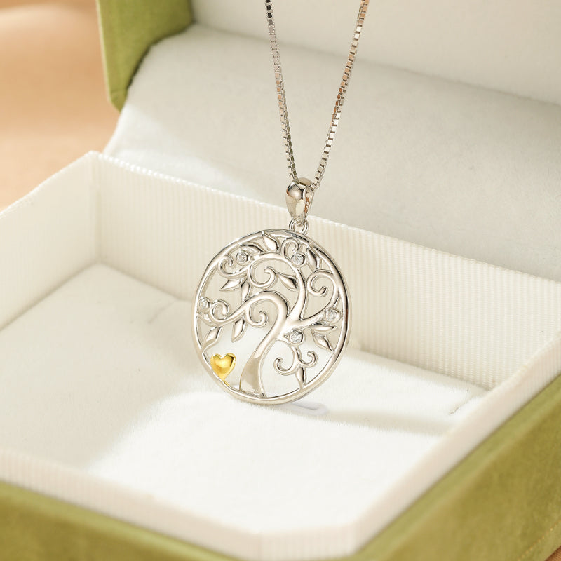 Collier Arbre de Vie en argent 925 orné de petits cristaux et d'un cœur doré, posé sur un écrin vert.