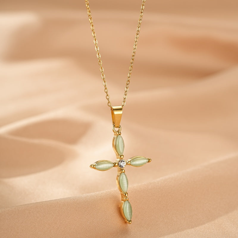 Collier en or avec un pendentif en forme de croix sertie de pierres d'aventurine ovales et d'une petite pierre transparente au centre, sur un fond satiné beige.