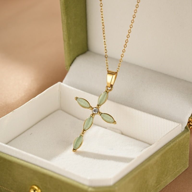 Collier plaqué or avec un pendentif croix orné de pierres vertes ovales et d'un cristal scintillant au centre, présenté dans une boîte cadeau verte.