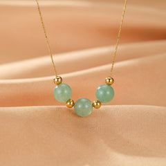 Collier plaqué or avec trois perles rondes d'aventurine verte pâle, espacées par de petites perles dorées, sur un fond en tissu satiné beige.