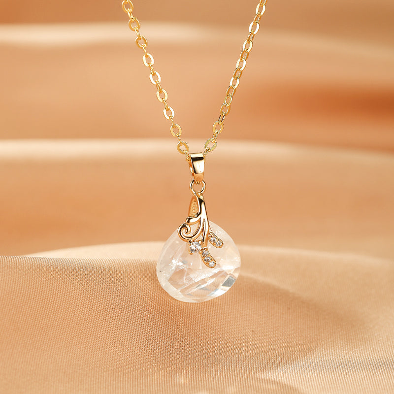 Collier "Bonheur Céleste" avec pendentif en cristal de roche brut en forme de goutte, monté sur une chaîne dorée et orné d'une breloque ajourée sertie de petits zircons.