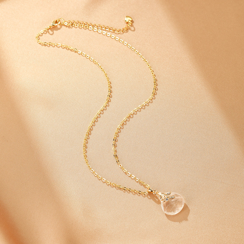 Collier fin plaqué or avec un pendentif en forme de goutte de cristal de roche transparent, orné de petites pierres bleues discrètes. La chaîne est délicate et ajustable.
