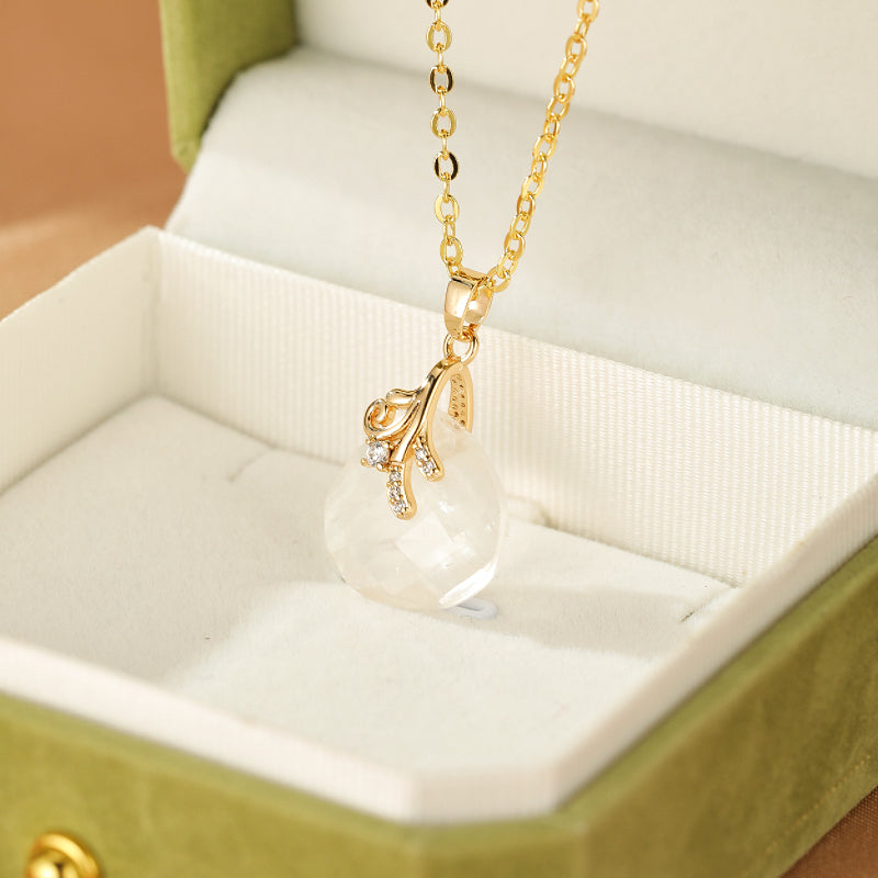 Collier "Bonheur Céleste" en cristal de roche avec pendentif goutte facetté et monture dorée ornée de cristaux, présenté dans un écrin vert.
