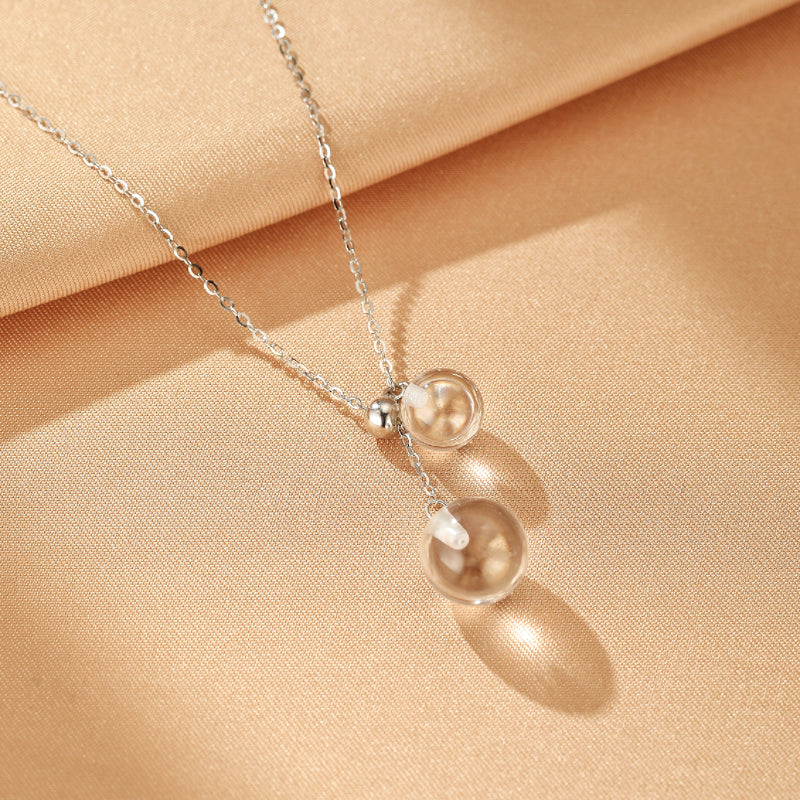 Collier en argent avec une chaîne délicate et deux pendentifs sphériques en cristal de roche transparent qui diffusent la lumière.