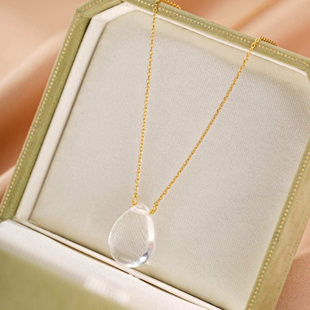 Collier en argent avec pendentif en forme de larme de cristal de roche transparent, présenté dans une boîte à bijoux verte.