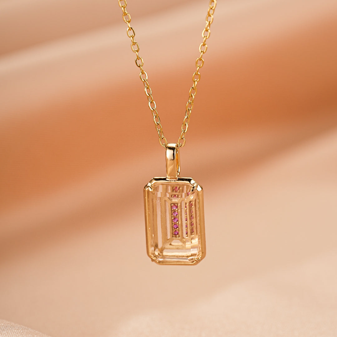 Collier plaqué or jaune avec un pendentif rectangulaire en cristal de roche incrusté de petites pierres roses.