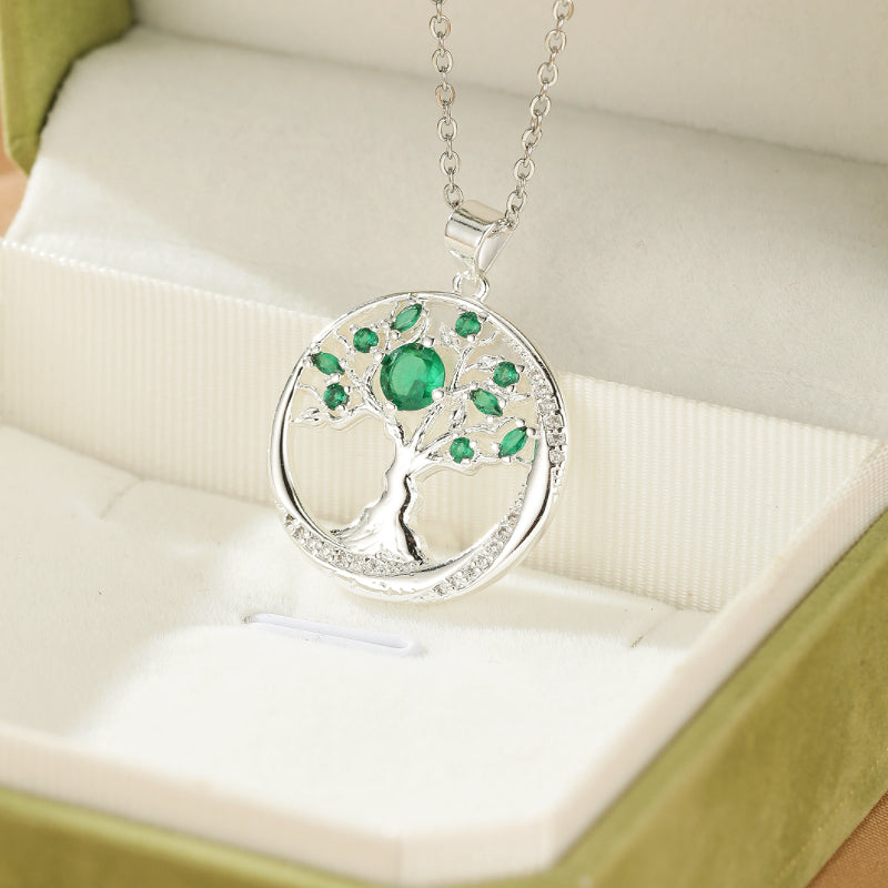 Collier Arbre Éternel en argent avec un pendentif rond orné d'émeraudes vertes et de cristaux incrustés, suspendu à une fine chaîne.