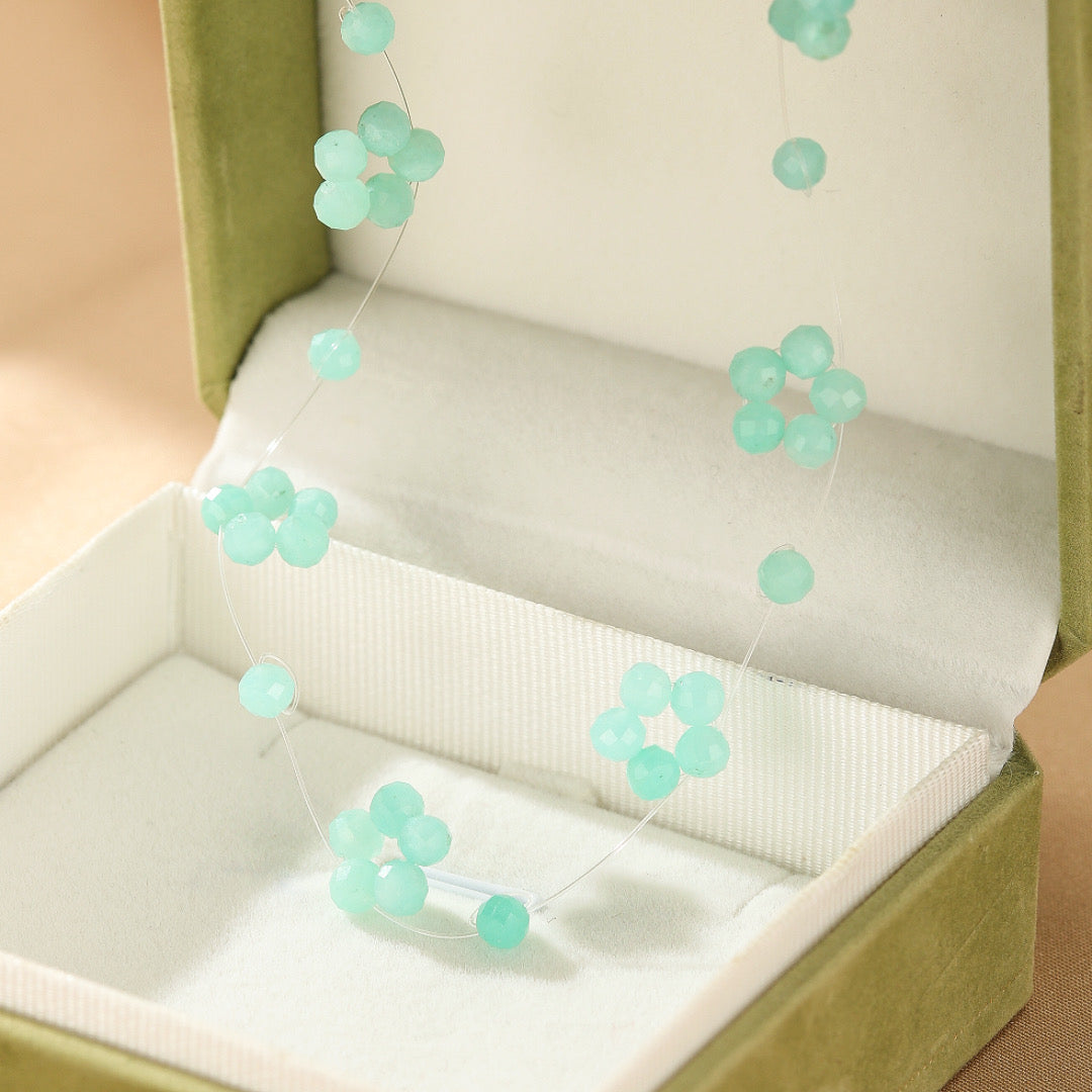 Collier flottant Fleur du Ciel avec perles en amazonite naturelle formant des fleurs délicates sur un fil transparent dans un écrin vert