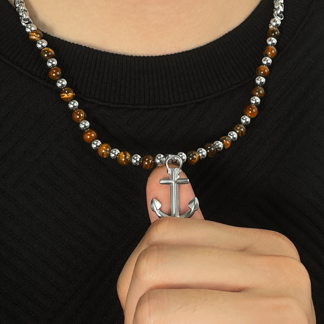 Collier pour homme avec un pendentif ancre marine en argent et des perles œil de tigre, gros plan sur la chaîne.