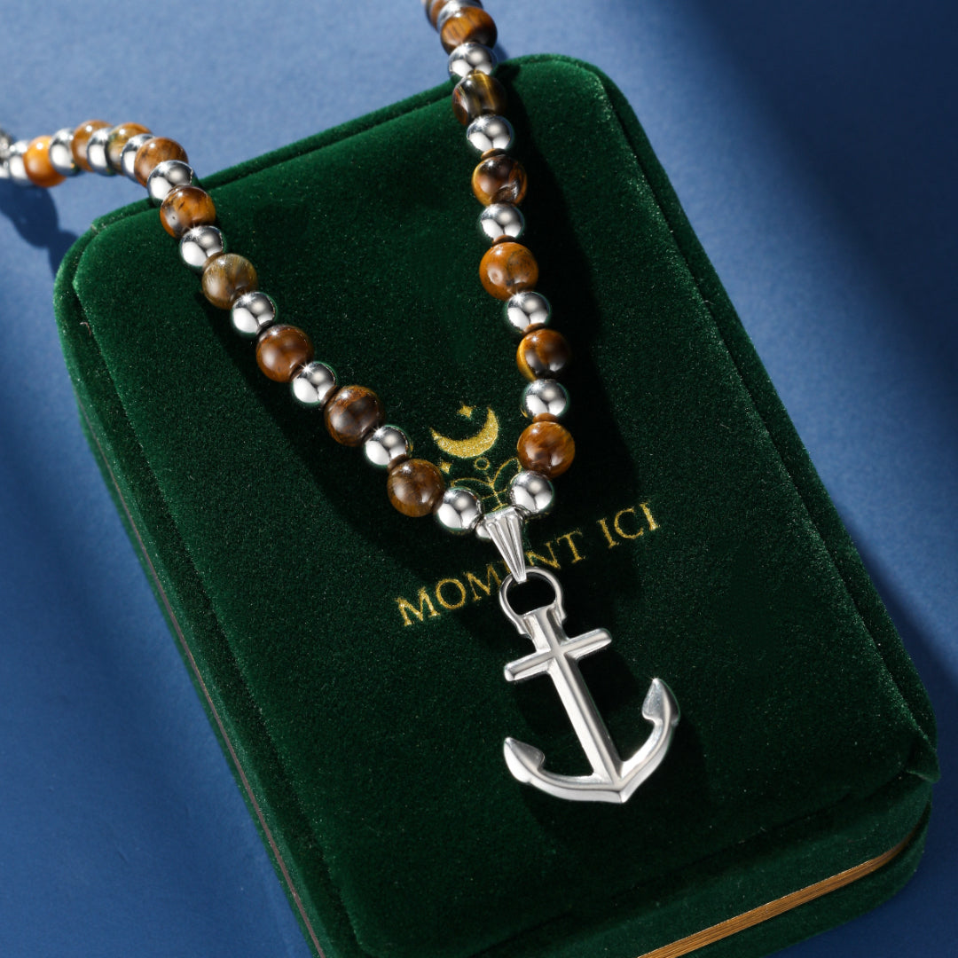 Collier homme avec perles œil de tigre et pendentif ancre marine argenté, sur boîte verte.
