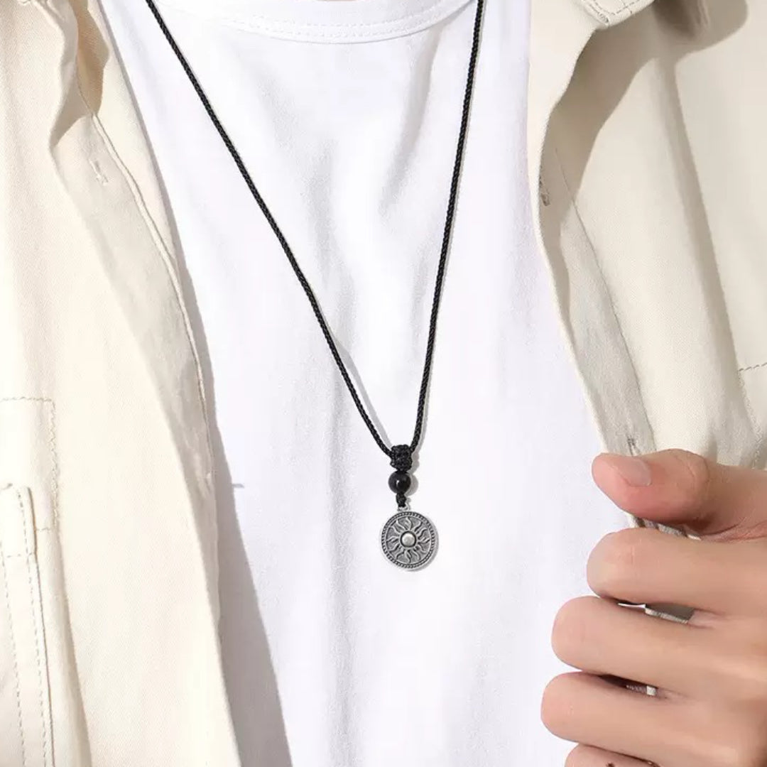 Collier homme avec pendentif rond gravé d'un soleil stylisé, perle d'obsidienne et cordon noir.