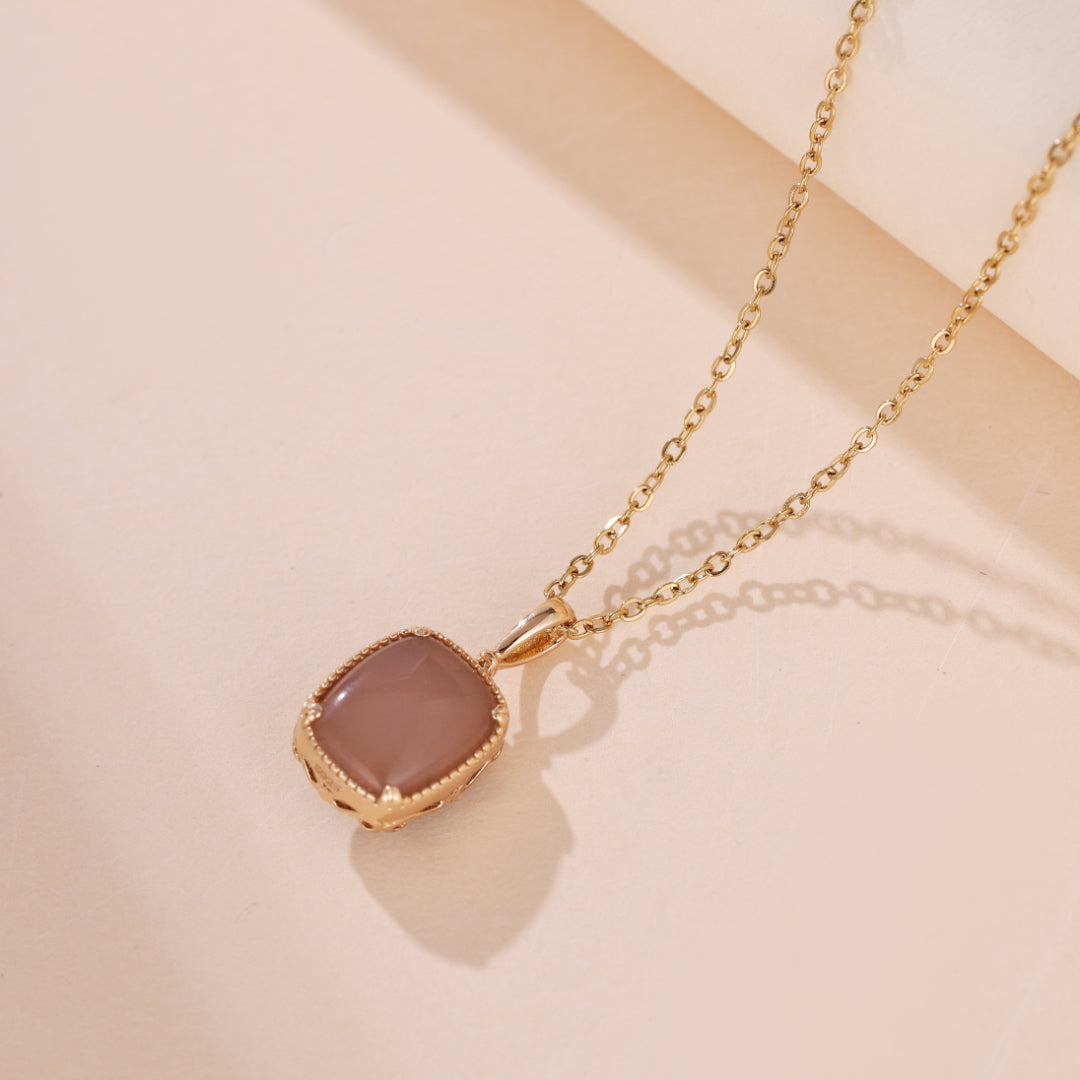 Gros plan d'un collier en argent plaqué or avec un pendentif carré en pierre de quartz rose, sur un fond clair.